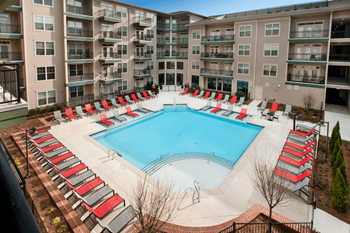an aerial view of a pool with red chaise lounge chairs and an apartment building in the